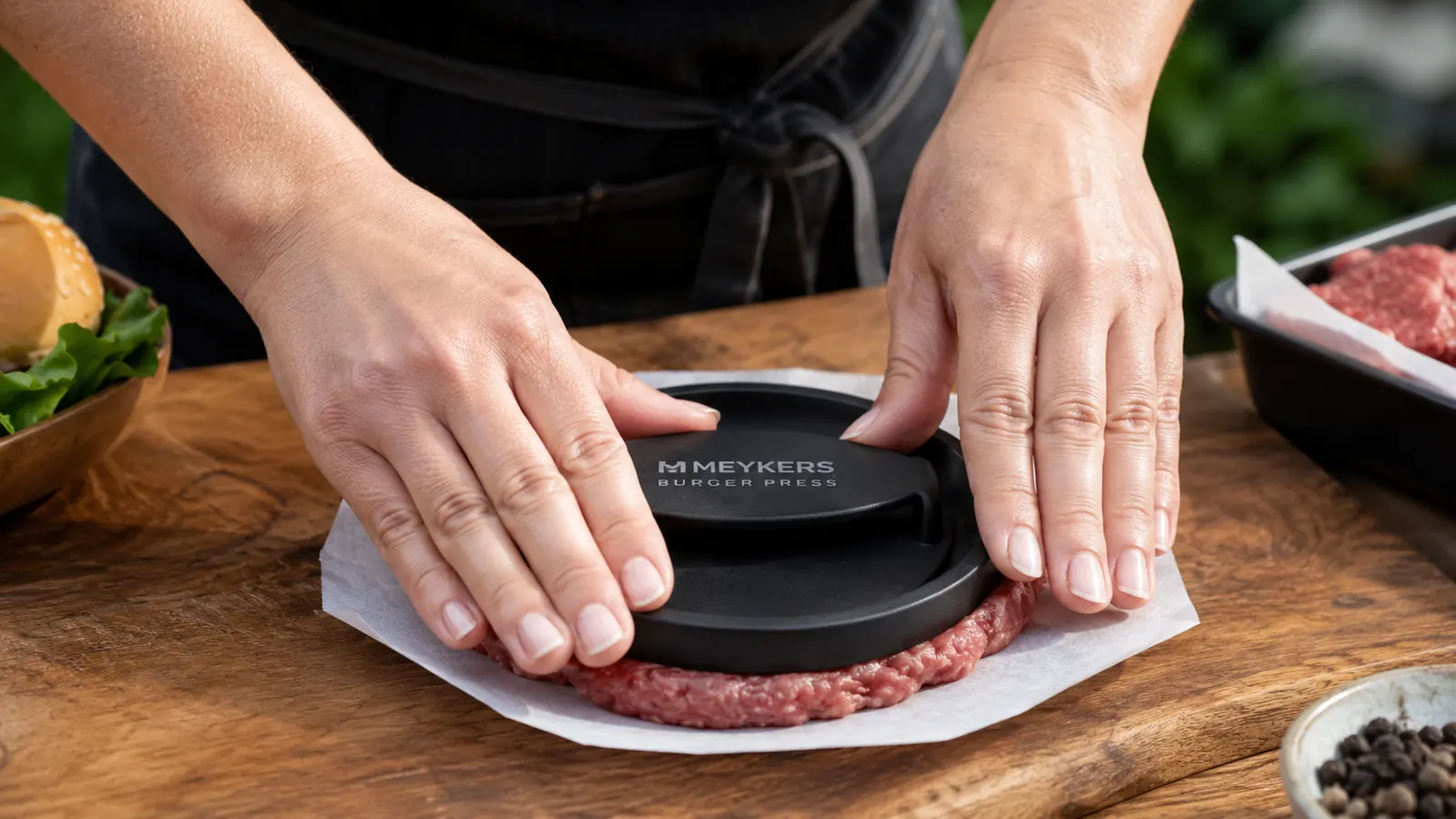 Hands using the Meykers burger press to form a patty on a sheet of wax paper