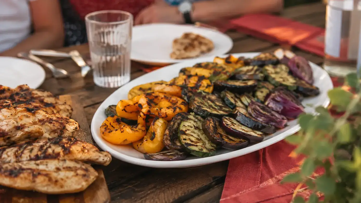 Finished grilled vegetables plated on a white serving dish next to grilled chicken at a backyard cookout