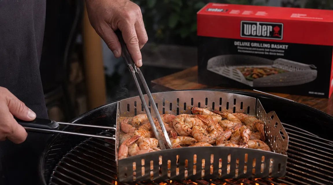 Hands using tongs to toss shrimp inside a Weber Deluxe Grilling Basket over a hot grill